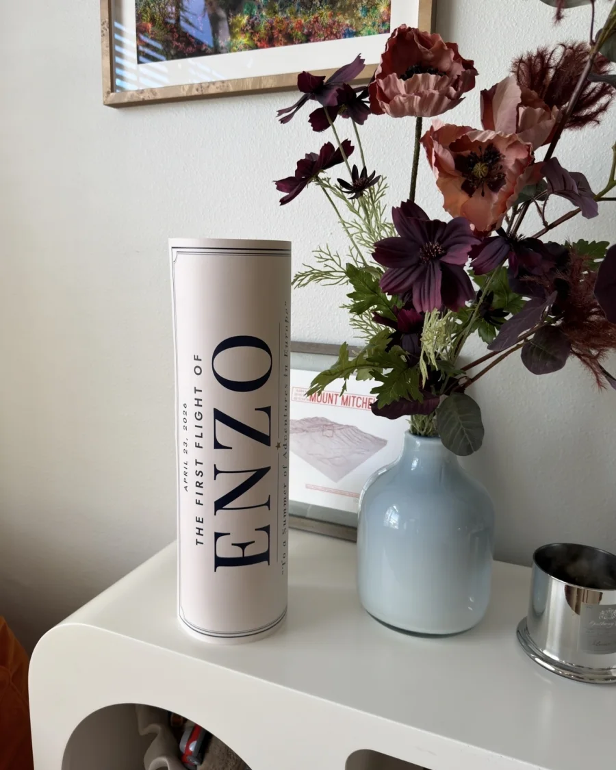 A personalized poster tube, “The first flight of Enzo”, beside a vase of flowers
